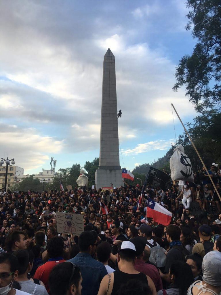 Manifestantes alrededor del obelisco ubicado al inicio del Parque Balmaceda para la marcha del 25 de octubre de 2019. Una persona escala el obelisco.