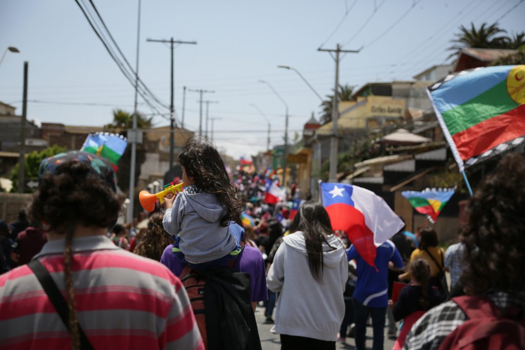 Marcha en Cartagena ocurrida el 25 de octubre de 2019, vista desde atrás. Niña lleva una trompeta de juguete. Flamean muchas banderas mapuche y chilenas.